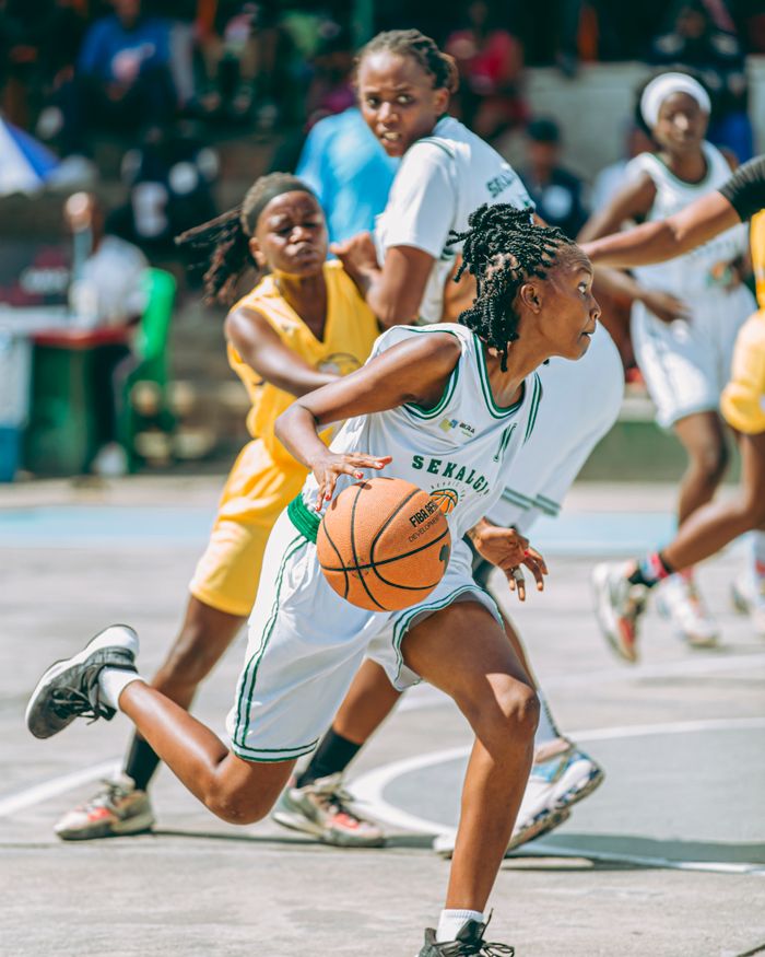 Dynamic image of women playing competitive basketball outdoors.